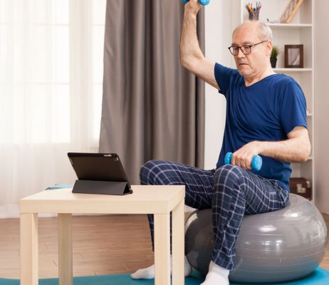 senior-man-doing-muscle-recovery-exercises-sitting-swiss-ball-front-tablet